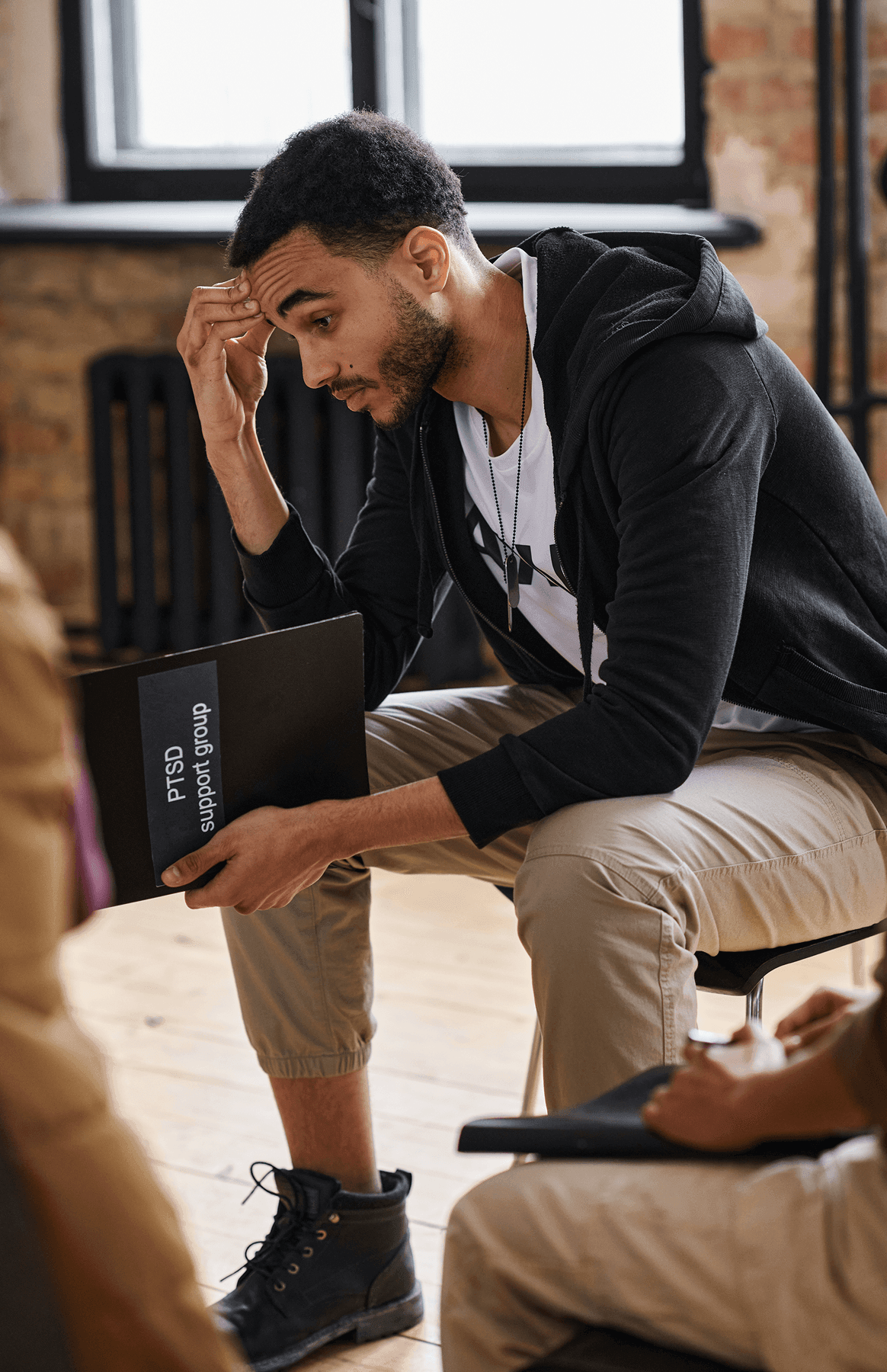 Man sitting, holding a folder, looking thoughtful.