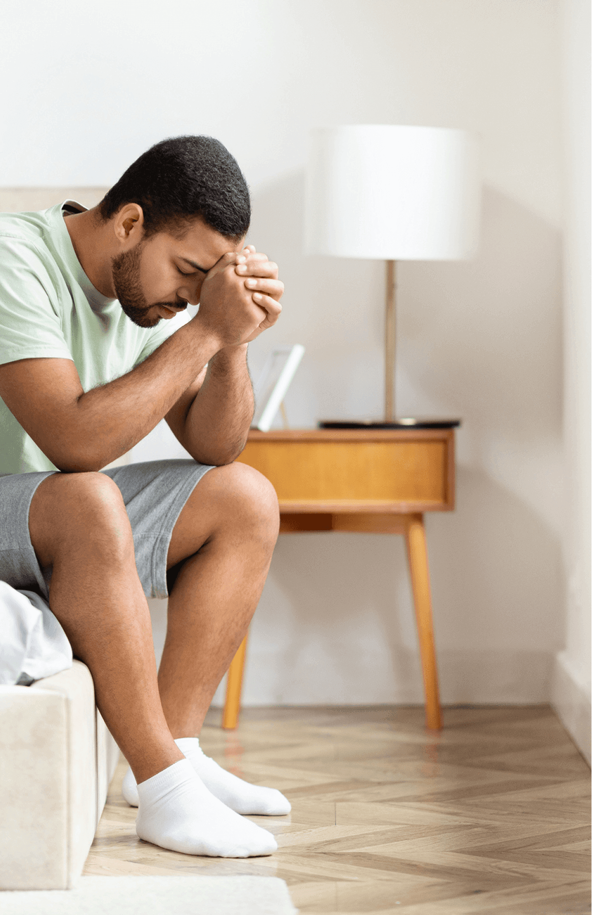 Man sitting on bed, deep in thought.
