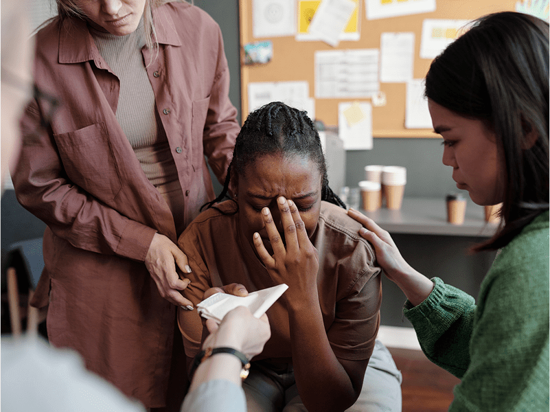 People comforting a distressed person with tissues.
